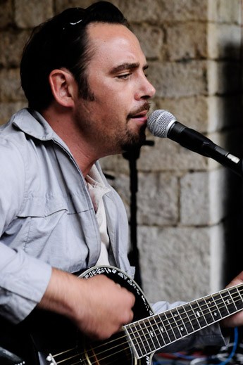 Musiker singt und spielt Gitarre vor einer historischen Steinwand